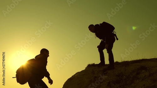 Climbers silhouettes stretch their hands to each other, climbing to top of hill. teamwork of business people. travelers climb one after another on rock. A team of businessman is going to win.