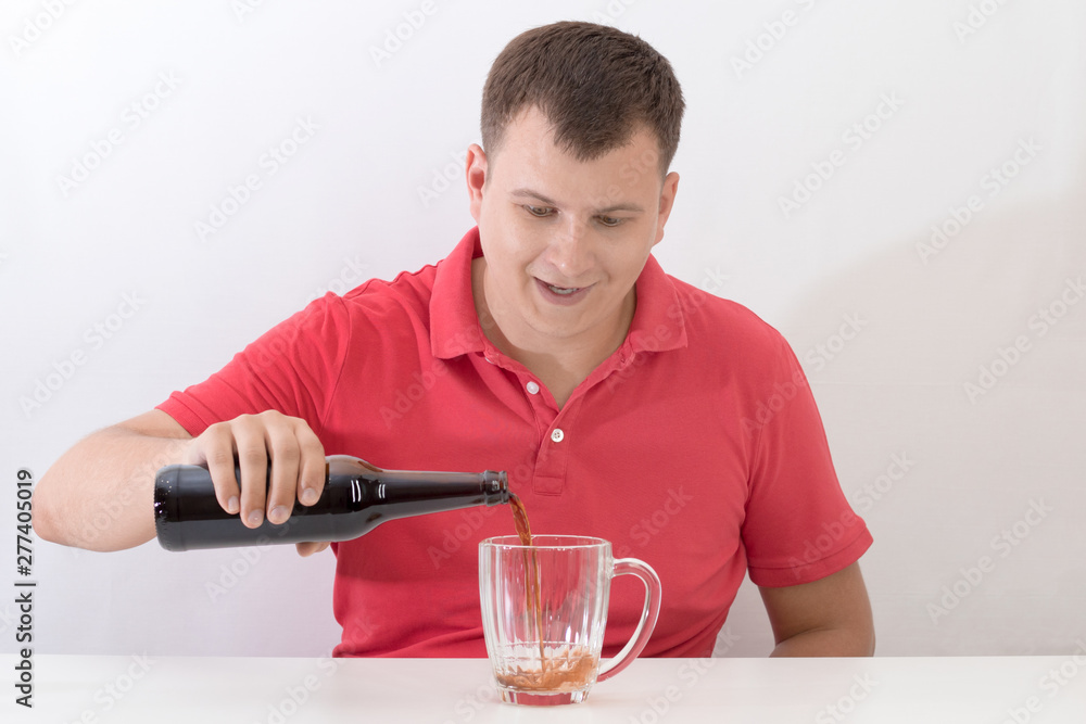 Happy man pouring a dark beer into a mug from a glass bottle Happy man pouring a dark beer into a mug from a glass bottle