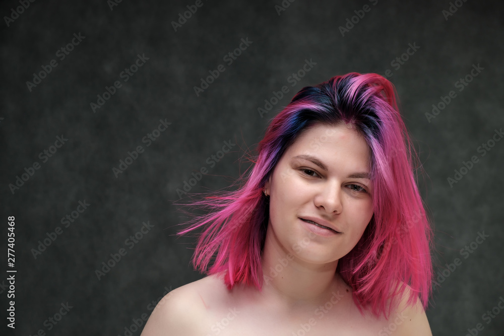 Naklejka premium Close-up portrait of a young pretty teen girl with beautiful purple hair on a gray background in the studio. Smiles with emotions