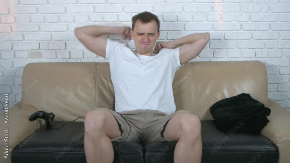 Caucasian young handsome man sitting on the beige couch and playing video games, then winning. At home. Close up portrait. Caucasian young handsome man sitting on the beige couch and playing video games, then winning. At home. Close up portrait.