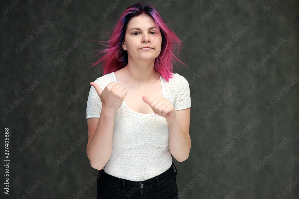 Portrait to waist of a young beautiful girl teenager in a white T-shirt with beautiful purple hair on a gray background in the studio. They say, they smile, they show hands with emotions. Portrait to waist of a young beautiful girl teenager in a white T-shirt with beautiful purple hair on a gray background in the studio. They say, they smile, they show hands with emotions.