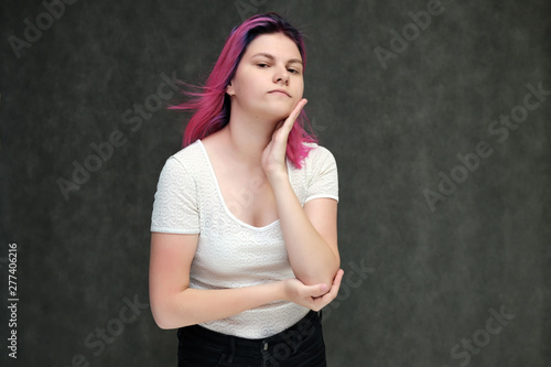 Portrait to waist of a young beautiful girl teenager in a white T-shirt with beautiful purple hair on a gray background in the studio. They say, they smile, they show hands with emotions.