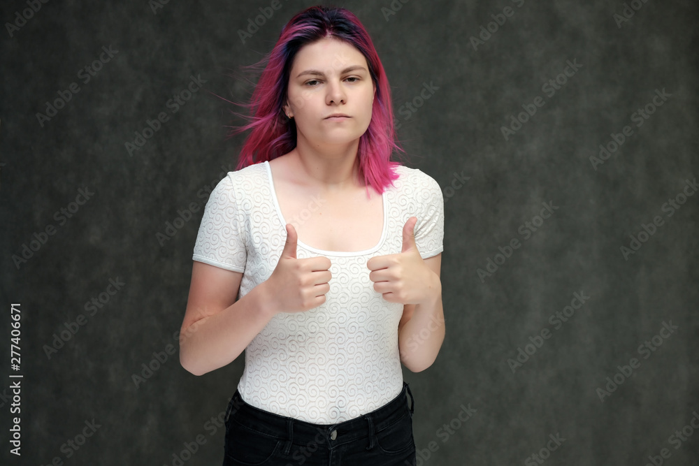 Portrait to waist of a young beautiful girl teenager in a white T-shirt with beautiful purple hair on a gray background in the studio. They say, they smile, they show hands with emotions. Portrait to waist of a young beautiful girl teenager in a white T-shirt with beautiful purple hair on a gray background in the studio. They say, they smile, they show hands with emotions.