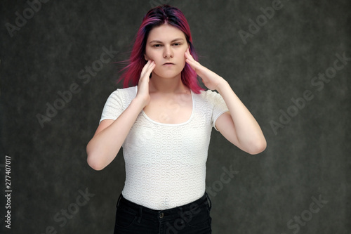 Portrait to waist of a young beautiful girl teenager in a white T-shirt with beautiful purple hair on a gray background in the studio. They say, they smile, they show hands with emotions.