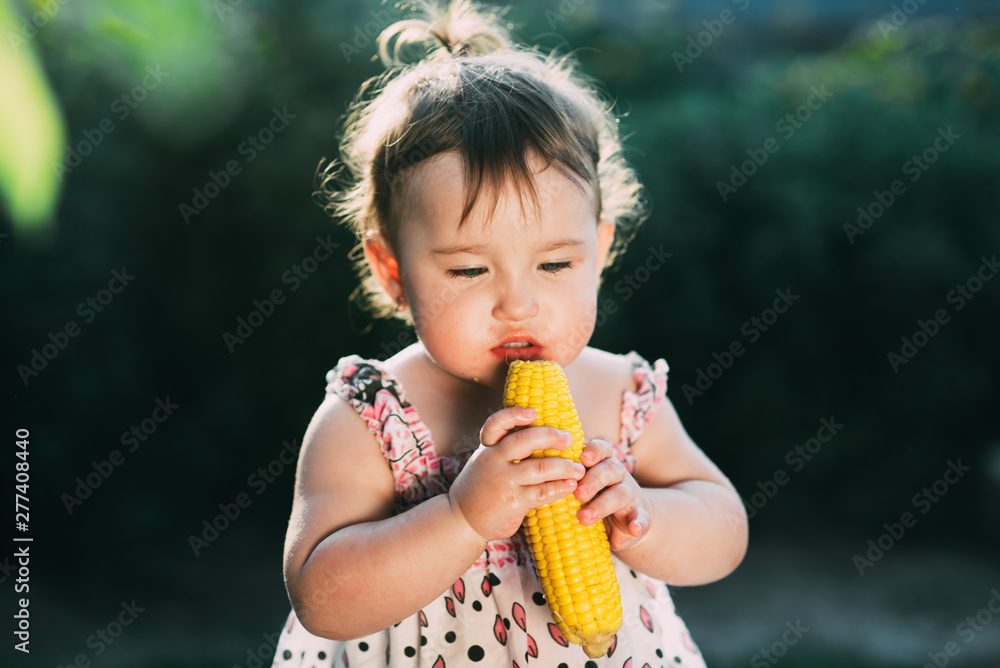 A little girl is holding boiled corn and thinking whether to eat or not A little girl is holding boiled corn and thinking whether to eat or not