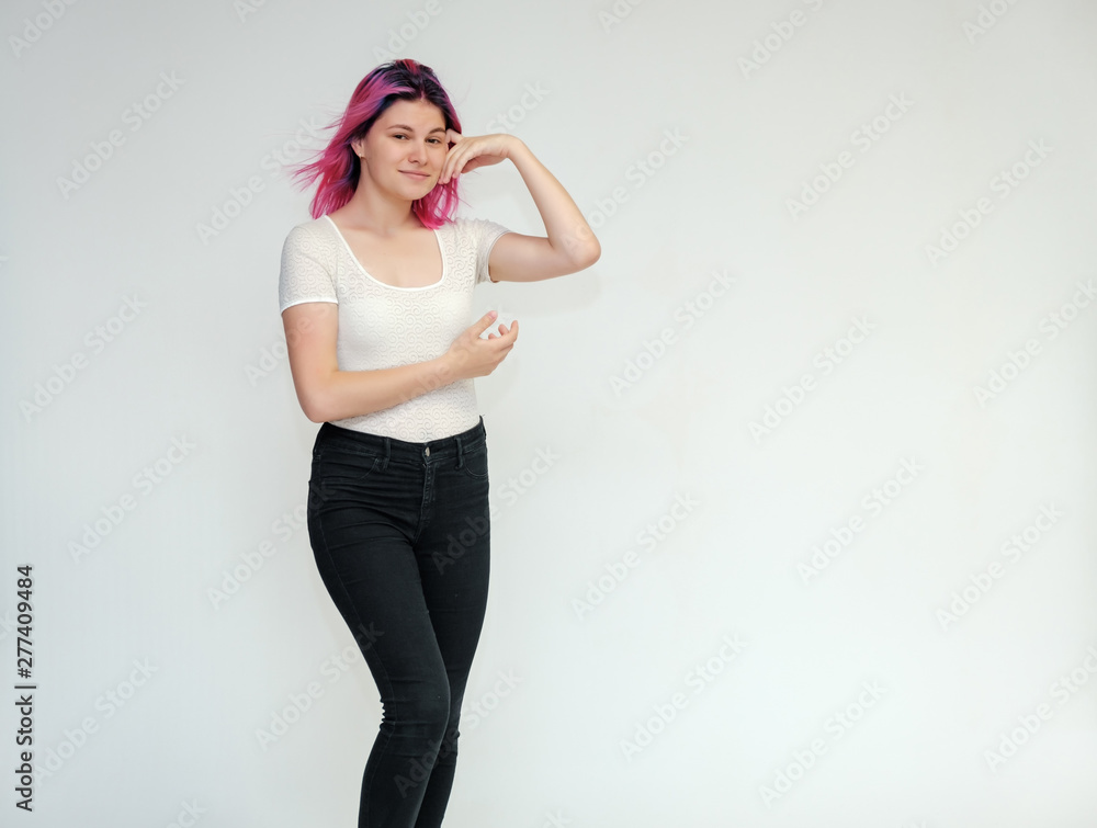 Portrait below the knee of a young beautiful girl teenager in a white T-shirt and black jeans with beautiful purple hair on a white background in the studio. They say, they smile, they show hands Portrait below the knee of a young beautiful girl teenager in a white T-shirt and black jeans with beautiful purple hair on a white background in the studio. They say, they smile, they show hands