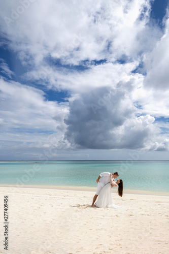 Newlyweds are passionately dancing on a gorgeous beach with white sand and turquoise water.