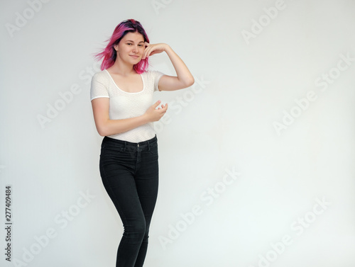 Portrait below the knee of a young beautiful girl teenager in a white T-shirt and black jeans with beautiful purple hair on a white background in the studio. They say, they smile, they show hands © Вячеслав Чичаев