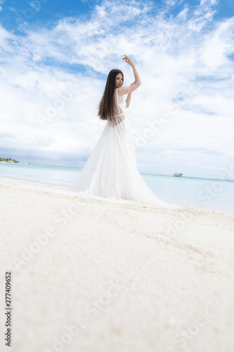 A young bride in a white dress is standing on a snow-white beach.