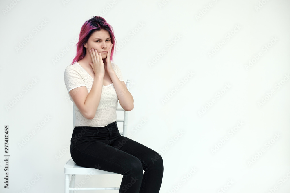 Portrait below the knee of a young beautiful girl teenager in a white T-shirt and black jeans with beautiful purple hair sitting on a white background in the studio. Says, shows hands with emotions. Portrait below the knee of a young beautiful girl teenager in a white T-shirt and black jeans with beautiful purple hair sitting on a white background in the studio. Says, shows hands with emotions.
