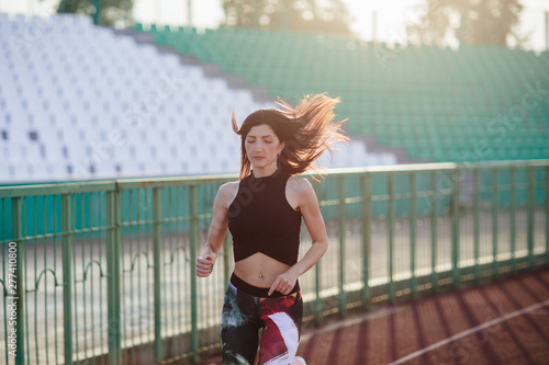 Obraz na płótnie Sport. Athletic young brunette woman in pink sneakers, leggings and top run on running track stadium at sunset. her hair is developing. Concept run. concept of a healthy lifestyle. w salonie