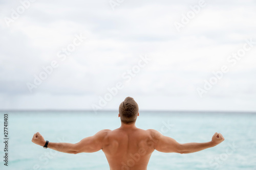 Inflated back and arms of a young guy on the background of the ocean and overcast sky