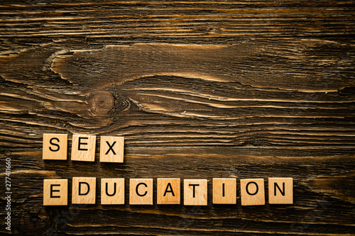 Sex education concept - letters, banana and condoms on wood background, top view