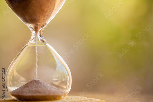 Sand running through the bulbs of an hourglass measuring the passing time in a countdown to a deadline with copy space.