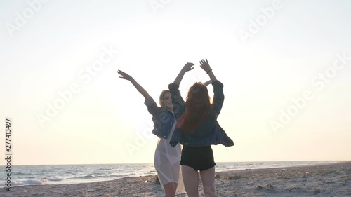 two young sexy women dressed in the style of boho rejoice and have fun in the rays of the sunset over the sea on the beach photo