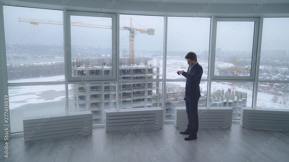young professional manager chatting with client or with boss check time on watch and hurry to a meeting. caucasian adult developer wearing in elegant suit in modern office with amazing view on the young professional manager chatting with client or with boss check time on watch and hurry to a meeting. caucasian adult developer wearing in elegant suit in modern office with amazing view on the