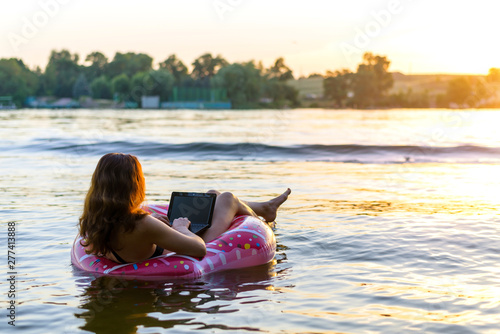 Young woman with laptop in the ring in the water during sunset, copy-space. © mihakonceptcorn