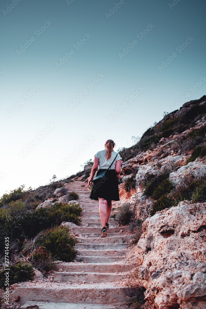 Fototapeta premium a young girl walking up stone stairs and hiking up the hill in the spanish natural landscape. Mallorca Spain Balearics