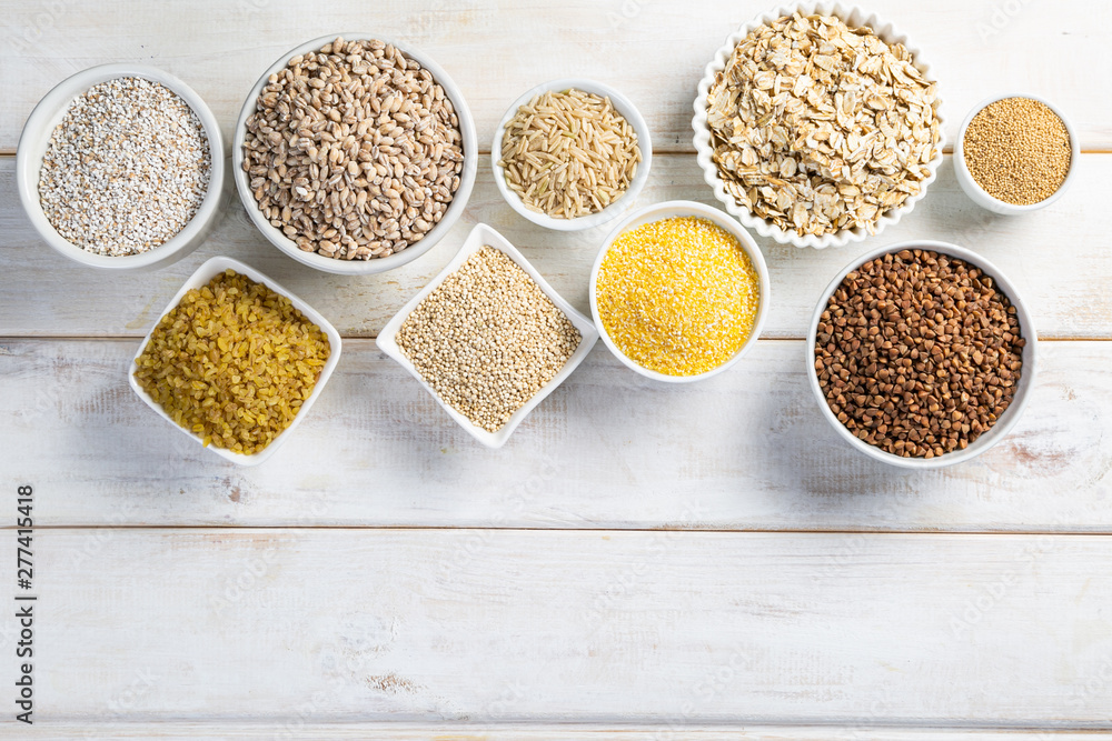 Selection of whole grains in white bowls - rice, oats, buckwheat, bulgur, porridge, barley, quinoa, amaranth, on white wood background Selection of whole grains in white bowls - rice, oats, buckwheat, bulgur, porridge, barley, quinoa, amaranth, on white wood background
