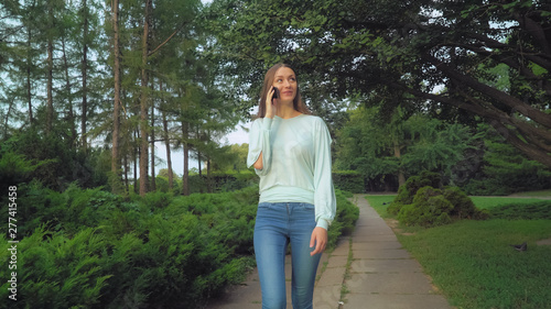 A young girl in a green blouse with long hair park talking and talking on the phone, smiles, surprised, enjoying the view.