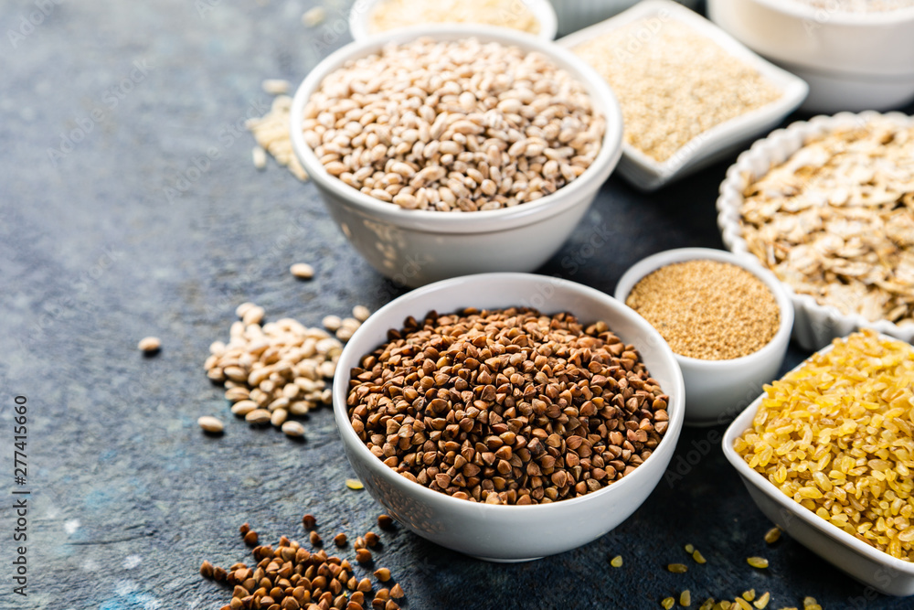Selection of whole grains in white bowls - rice, oats, buckwheat, bulgur, porridge, barley, quinoa, amaranth on dark background Selection of whole grains in white bowls - rice, oats, buckwheat, bulgur, porridge, barley, quinoa, amaranth on dark background