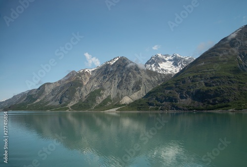 Blue sky, dark grey mountains, and teal ocean water meet in Alaska's Glacier National Park