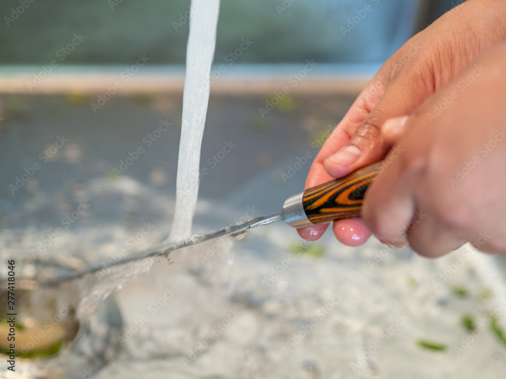 Obraz premium Man's hands washing under the tap a kitchen knife.