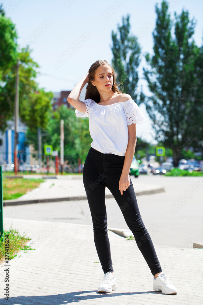 Young beautiful brunette woman in jeans and white blouse walking in summer street Young beautiful brunette woman in jeans and white blouse walking in summer street