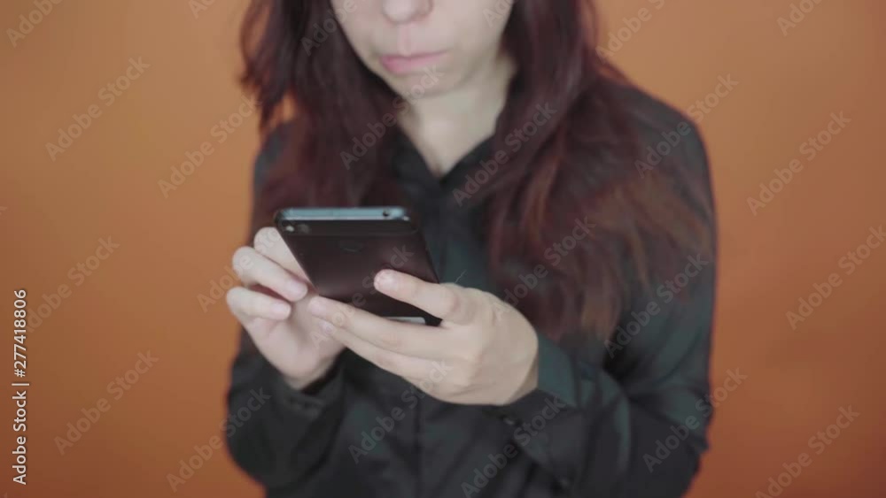 Young woman holding mobile phone in hand on orange background. Female typing a message on a smartphone Young woman holding mobile phone in hand on orange background. Female typing a message on a smartphone
