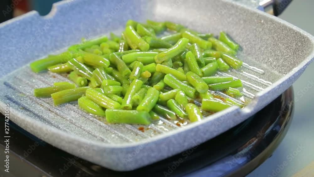 In a pan, green string beans are ground in oil and stirred with a wooden spatula In a pan, green string beans are ground in oil and stirred with a wooden spatula