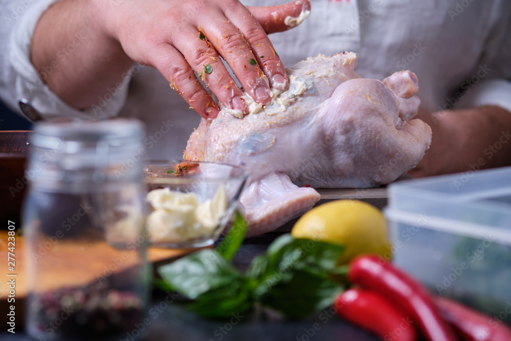 A man rubs chicken with butter. The process of cooking chicken with herbs, spices and lemon in the oven. On the table are the products that are needed for cooking. The hands of the cook in the frame.