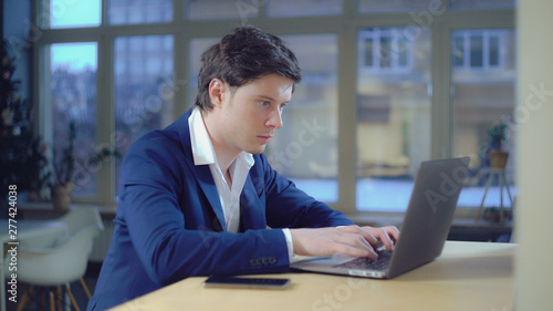 Portrait businessman focused on work. Handsome professional man typing fast on laptop. Caucasian model sitting at the desk indoors looking on screen computer.