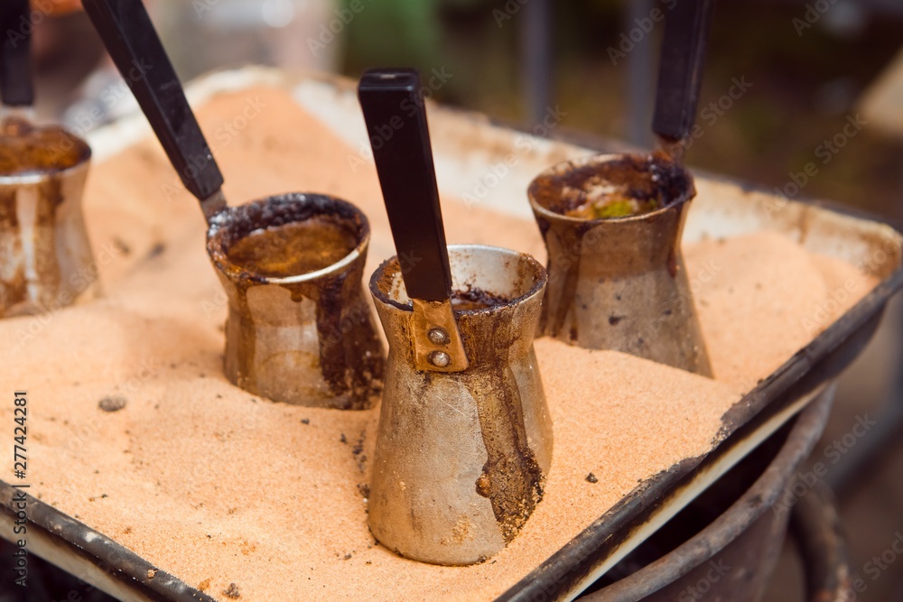 set of coffee pots with boiling coffee, turkish traditional recipe of cooking drink in sand, roadside coffee spot, close-up food photo set of coffee pots with boiling coffee, turkish traditional recipe of cooking drink in sand, roadside coffee spot, close-up food photo