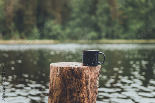 coffee mug on a stump on the bank of a lake or river. Breakfast at nature. Summer camp and hiking.