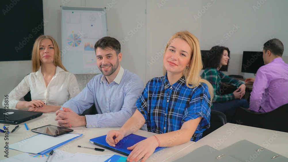 Obraz premium Staff closing laptop and looking at the camera with friendly smile. Young workers in startup company sitting in the modern contemporary office. Casual diverse people using digital device like laptop