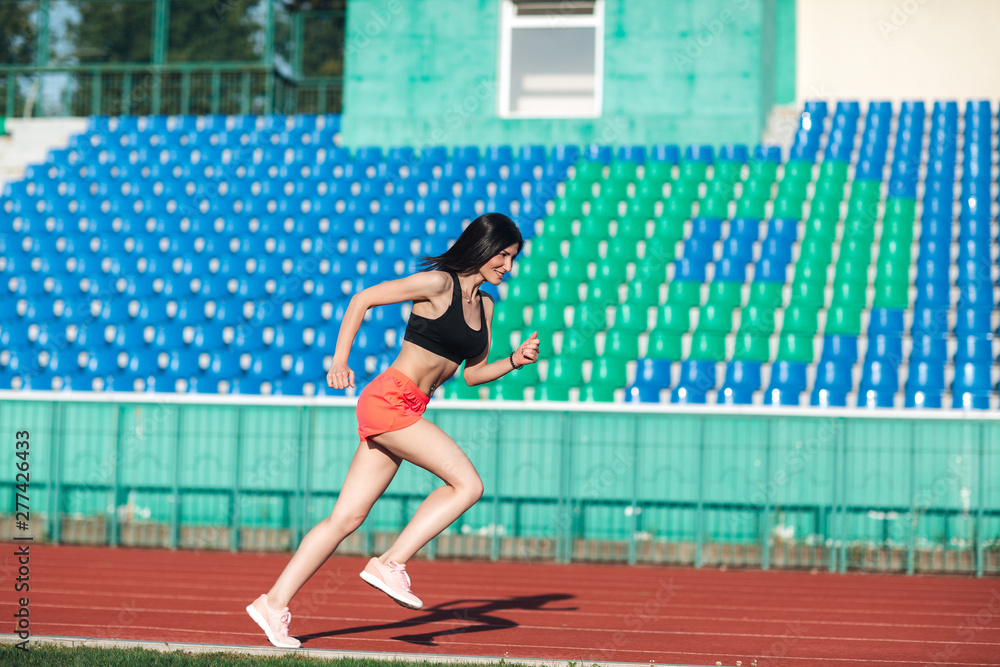 Sporty young brunette woman in pink shorts and tank top running at the stadium. Healthy active lifestyle. Summer sport activity.