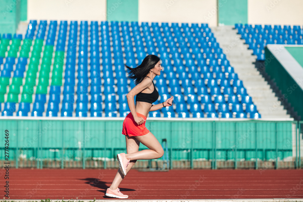 Girl running track on stadium. Real side view of young woman in pink shorts and tank top and pink sneakers. Outdoors, sport.
