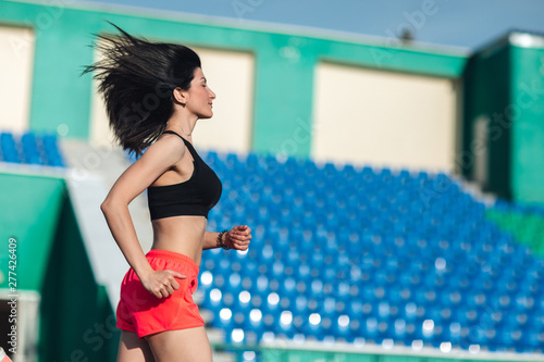 Obraz na płótnie Girl running track on stadium. Real side view of young brunette woman in pink shorts and tank top and pink sneakers. Outdoors, sport w salonie