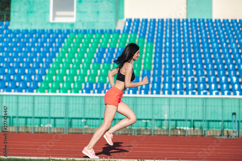 Obraz na płótnie Girl running track on stadium. Real side view of young woman in pink shorts and tank top and pink sneakers. Outdoors, sport w salonie