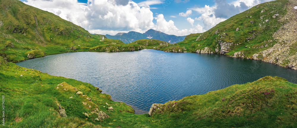 lake capra of romanian fagaras massif panorama. beautiful alpine scenery of carpathians in summer. clouds on the blue sky. grass and boulders on the slopes
