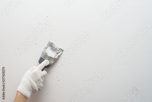 Working tool, spatula in hand against the background of a white wall, work plasterer. Putty walls with their own hands.