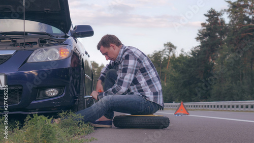 Man stuck on the side of the road with a flat tire. Caucasian driver change a tire at the roadside. © vadosloginov