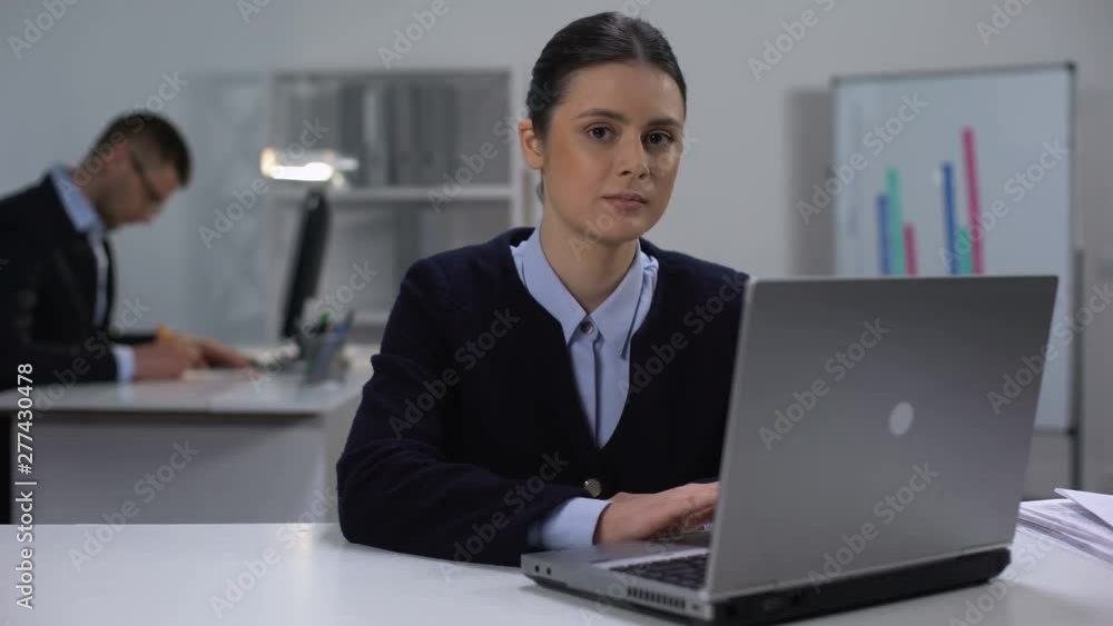 Female manager typing on laptop and smiling at camera, workday in big company Female manager typing on laptop and smiling at camera, workday in big company