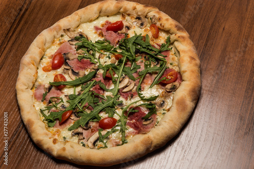 closeup of whole pizza with arugula, ham, mushrooms and tomatoes