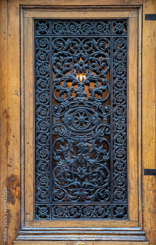 Old wooden door. Whimsical ornate gratings of vintage wooden door with framed door panel. Closeup of antique ornate metal lattice with backlight. Antique door in Paris France. Baroque architecture.