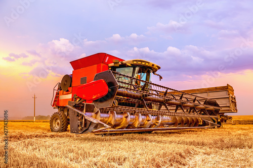 Combine harvester close-up. In the background is a bright  colorful sky of summer sunset.