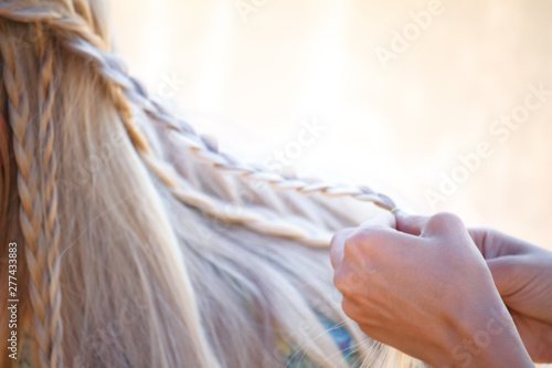 Close-up female graceful hands tangle blond hair in small pigtails