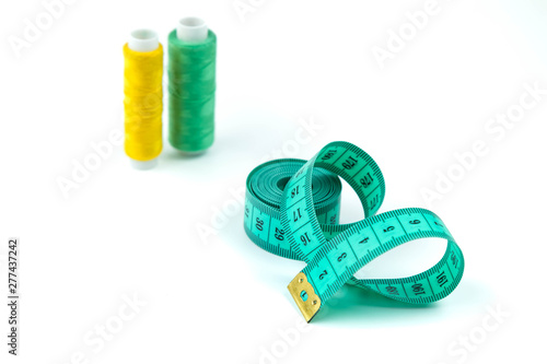 Set of sewing accessories: The green measuring centimetric tape curtailed by a spiral on a white background and coils with strings of yellow and green colors photo