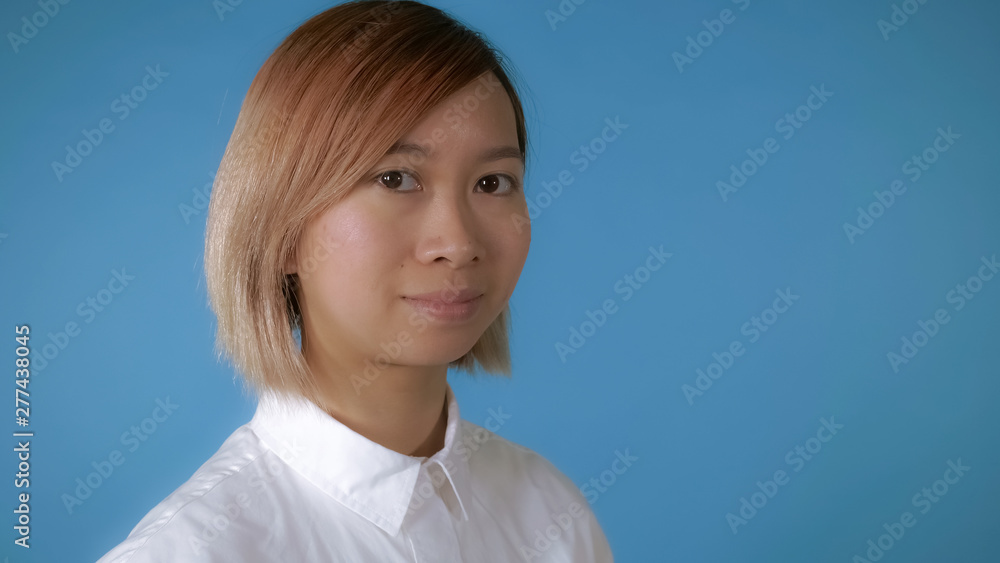 close up face young asian businesswoman posing on blue background in studio. attractive korean woman with blond hair wearing white casual shirt looking at the camera close up face young asian businesswoman posing on blue background in studio. attractive korean woman with blond hair wearing white casual shirt looking at the camera