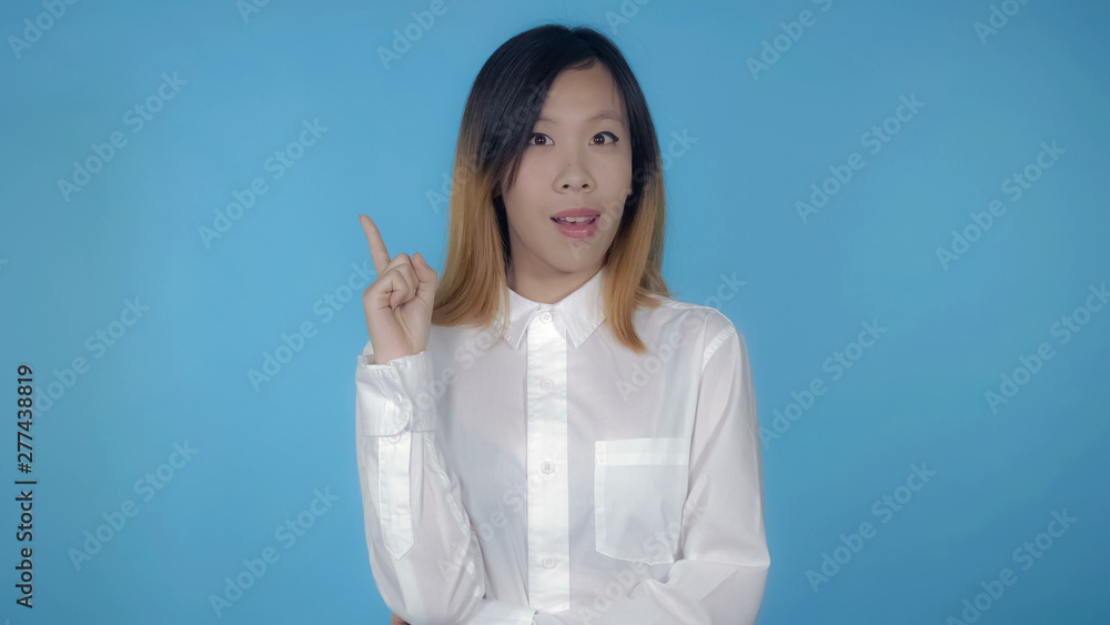 young asian woman posing showing hand gesture find decision on blue background in studio. attractive millennial girl wearing white casual shirt looking at the camera young asian woman posing showing hand gesture find decision on blue background in studio. attractive millennial girl wearing white casual shirt looking at the camera